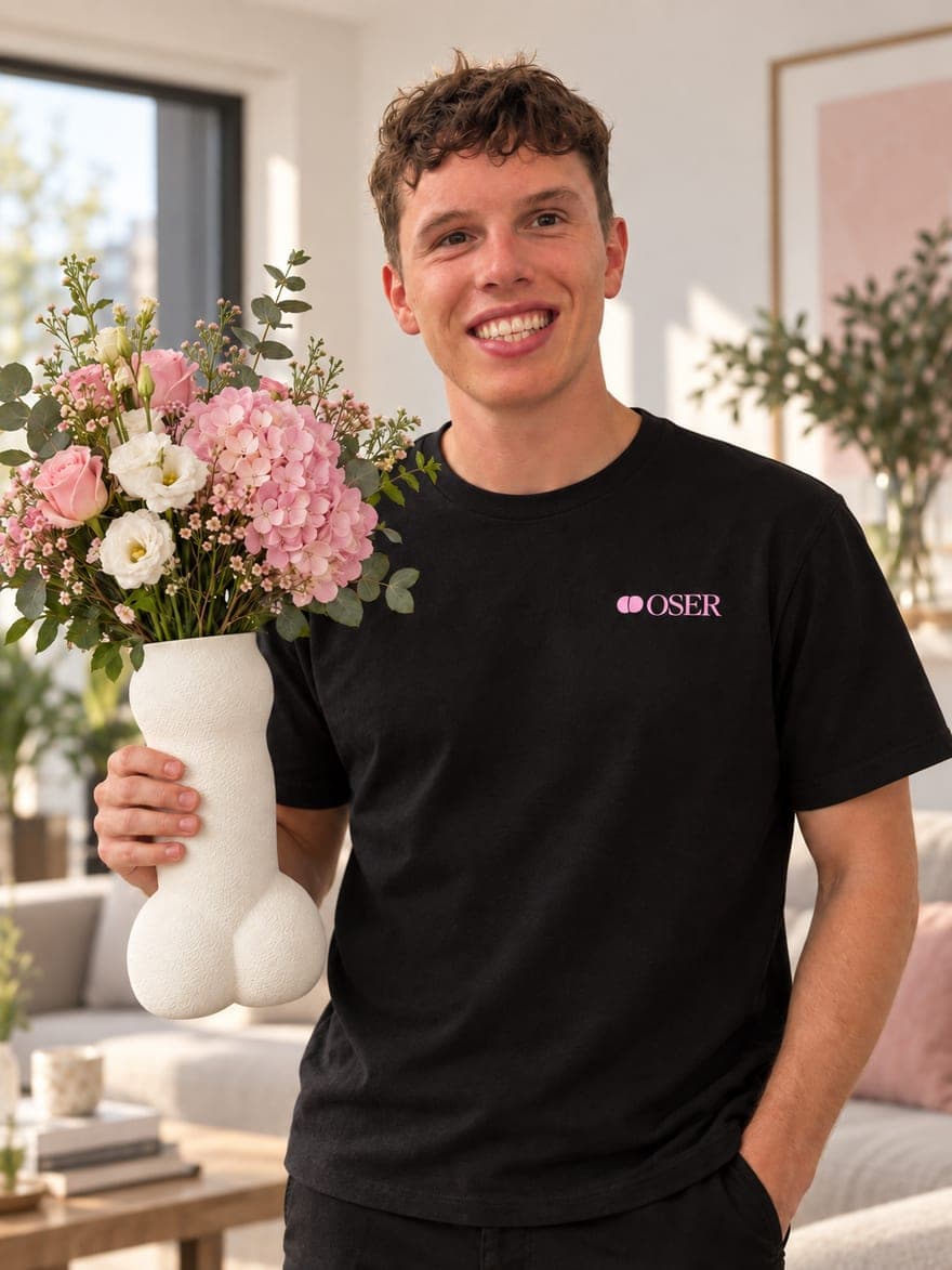 Un membre de l'atelier OSER, en t-shirt noir au logo de la maison, tient le Vase Flora blanc garni d'un bouquet de roses et d'hortensias roses dans un salon clair